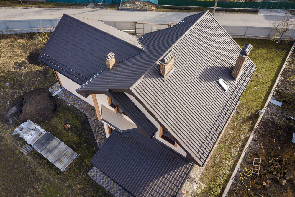 Aerial view of a modern two-story house with a dark metal roof, multiple chimneys, and surrounding yard space.